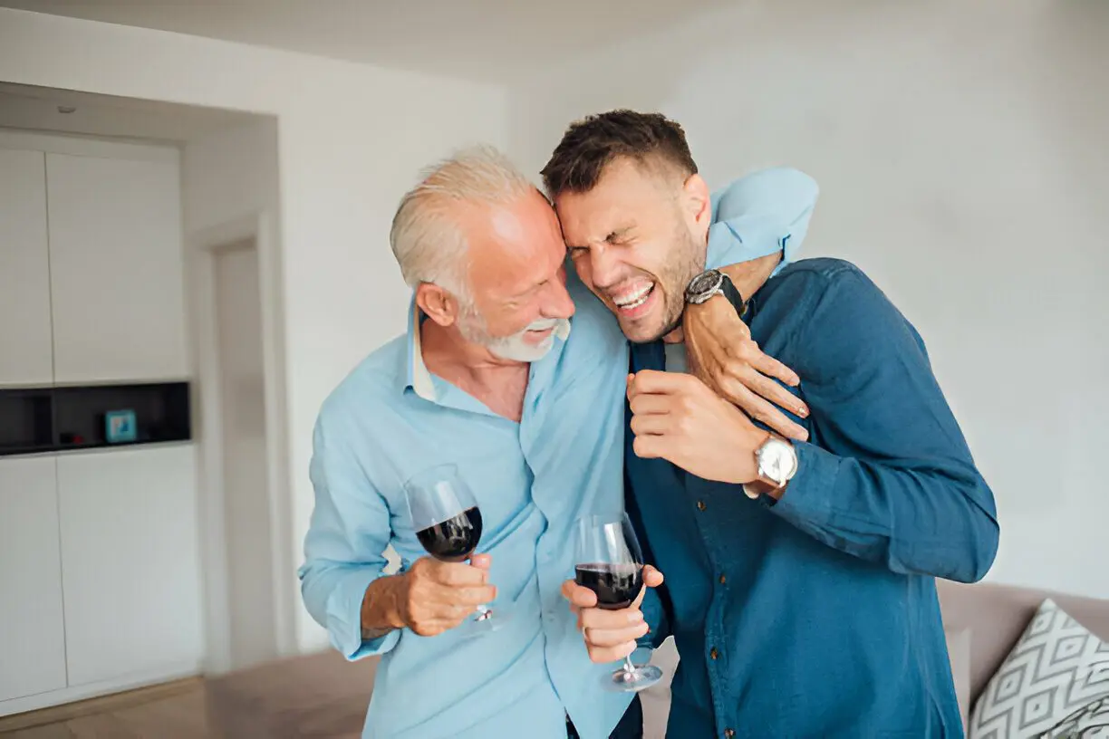 Two men are holding wine glasses and laughing.
