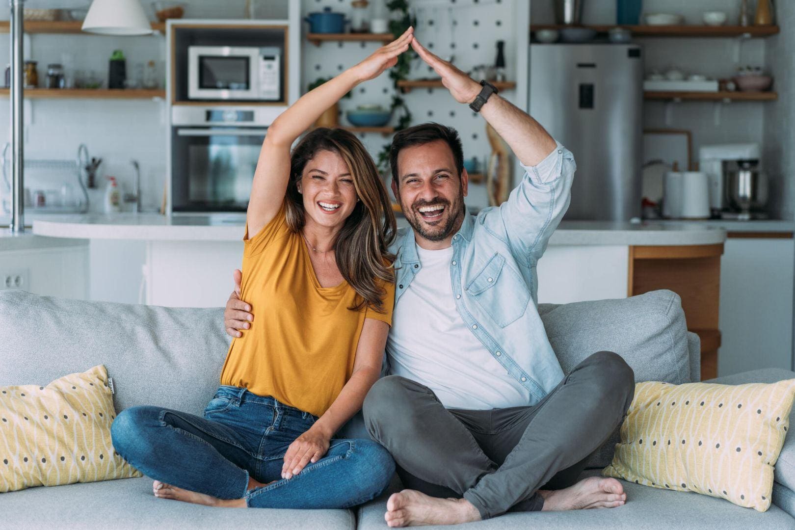 A man and woman sitting on the couch with their hands in the air.