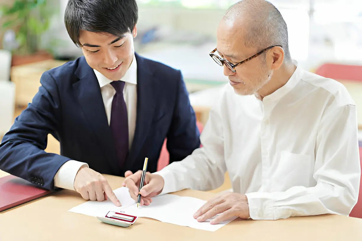 Professional financial advisor helping an elderly man sign legal paperwork.